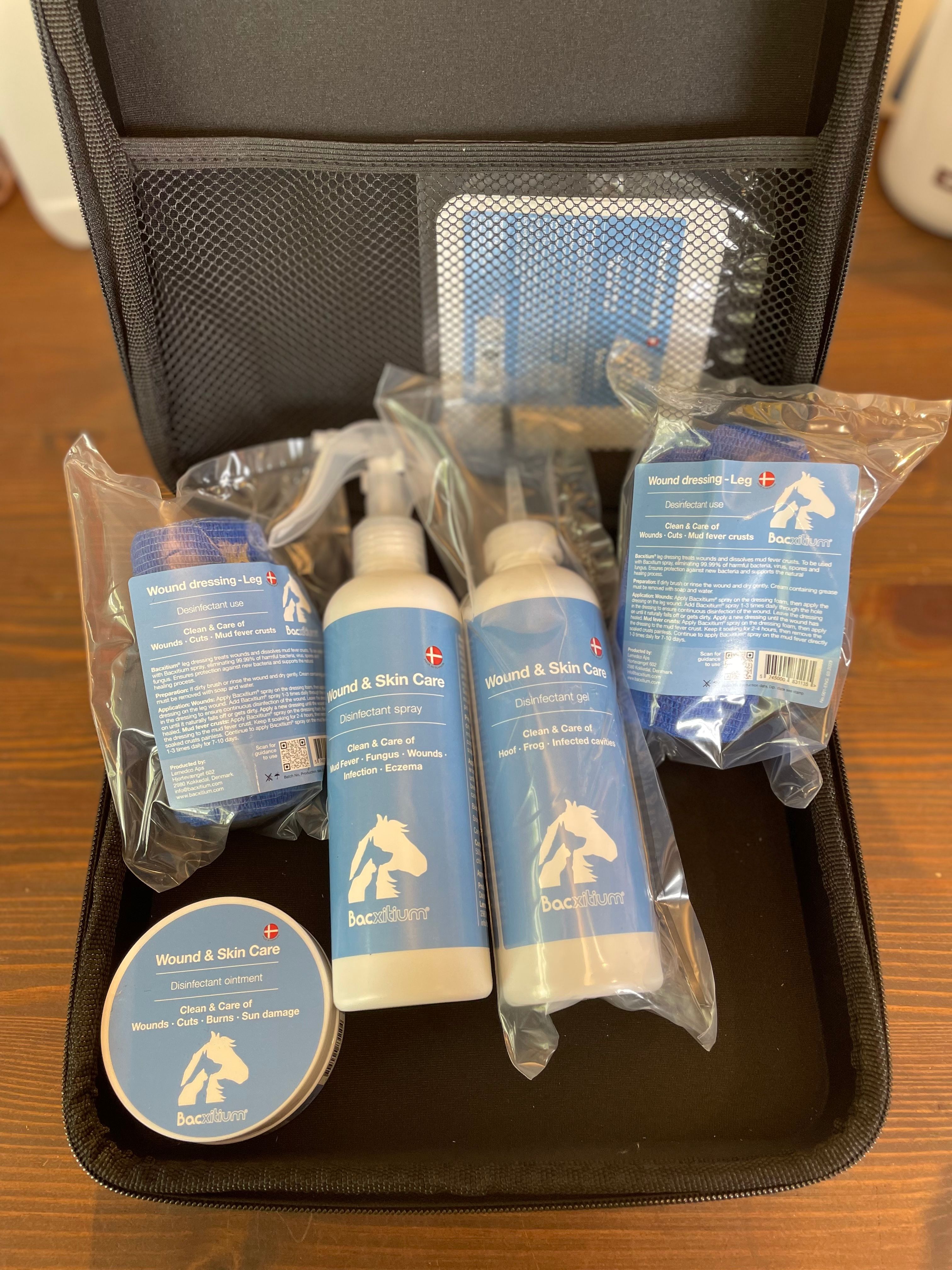 Geöffnete schwarze Tasche mit verschiedenen Produkten. Enthalten sind Sprays, Gel, Bandagen und eine Creme. Beschriftung: Bacxitium®.