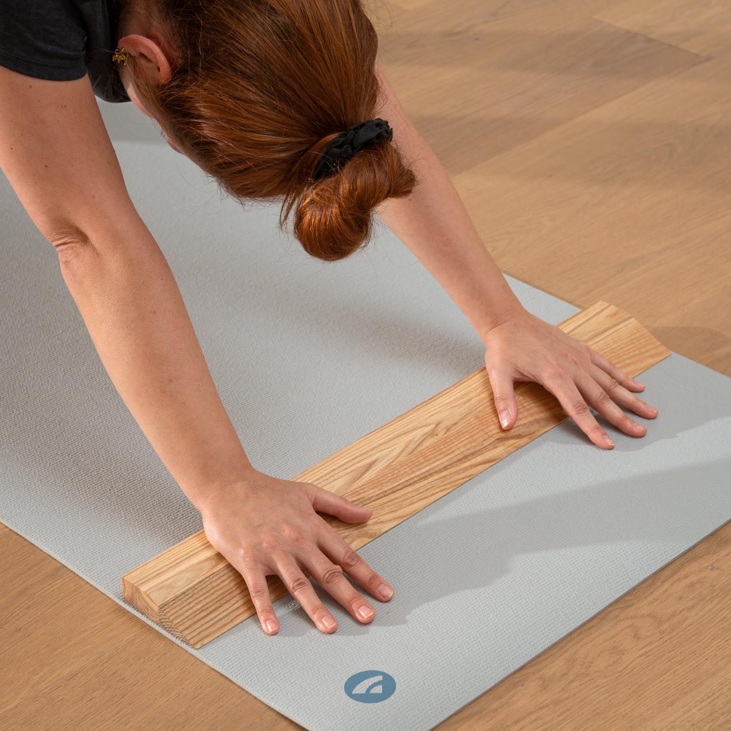 Person mit Handstandplanke auf Yogamatte. Hellbraunes Holz. Graue Matte. Person in Yoga-Position.