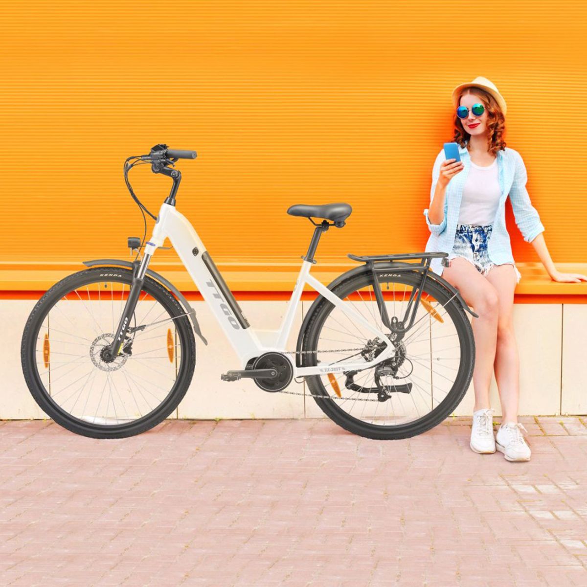 Eine Frau sitzt neben einem weißen E-Bike. Das Fahrrad hat schwarze Reifen und einen Gepäckträger.