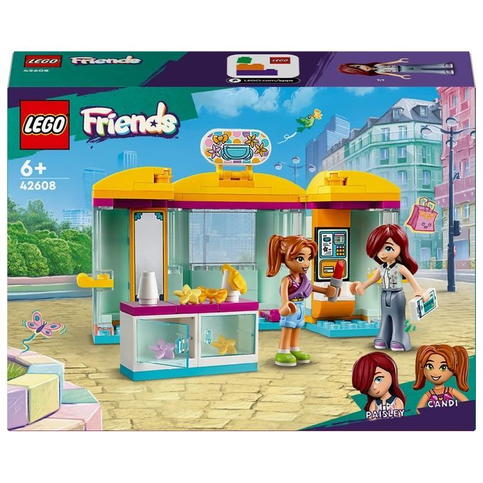 Set LEGO Friends 42608. Il set mostra un piccolo negozio con personaggi. Include una facciata gialla e rosa, due personaggi e accessori. Sulla confezione è scritto "6+".