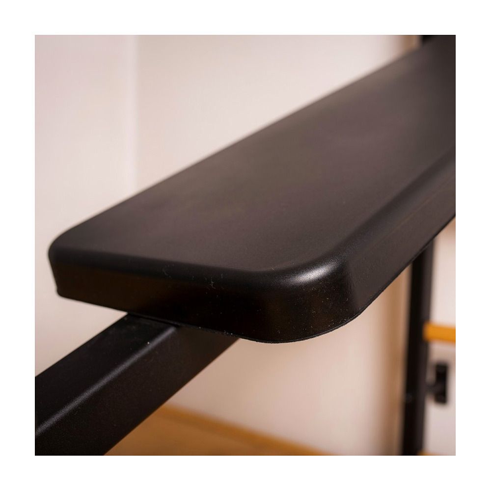 Schwarze Trainingsbank, Detailansicht der Sitzfläche. Gepolsterte Oberfläche. Metallrahmen. Helle Wand im Hintergrund.