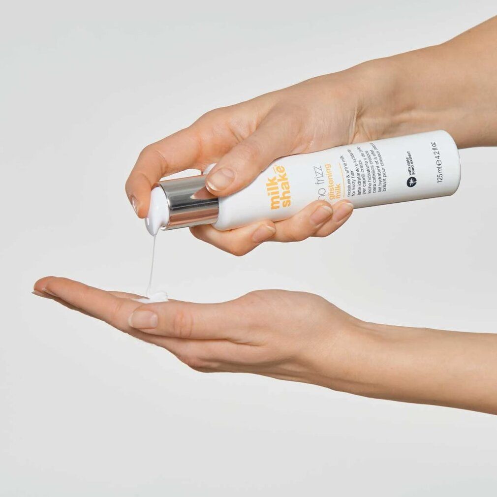 Hände halten eine weiße Flasche mit Pumpe. Produkt wird auf die Handfläche gedrückt. Aufschrift: Milk_Shake, No Frizz Glistening Milk.