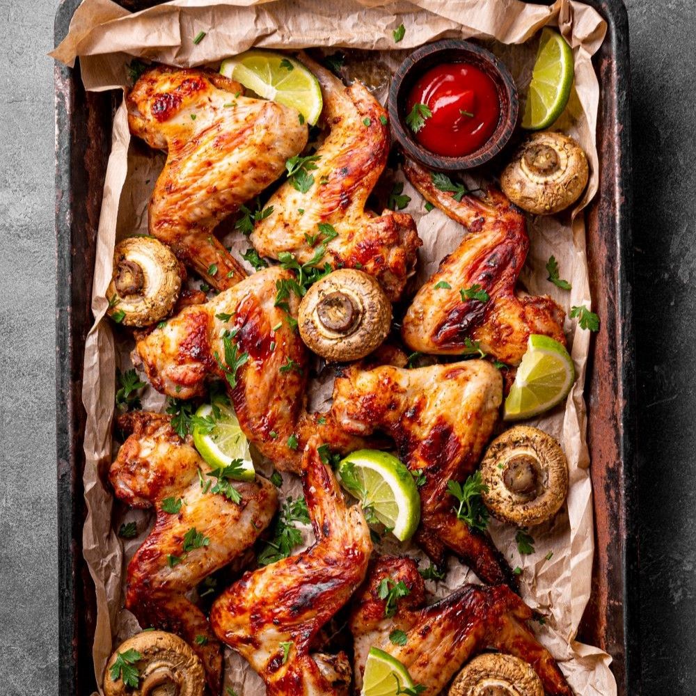 Gebratene Hähnchenflügel, Limettenscheiben, Pilze und Ketchup in einer Backform.