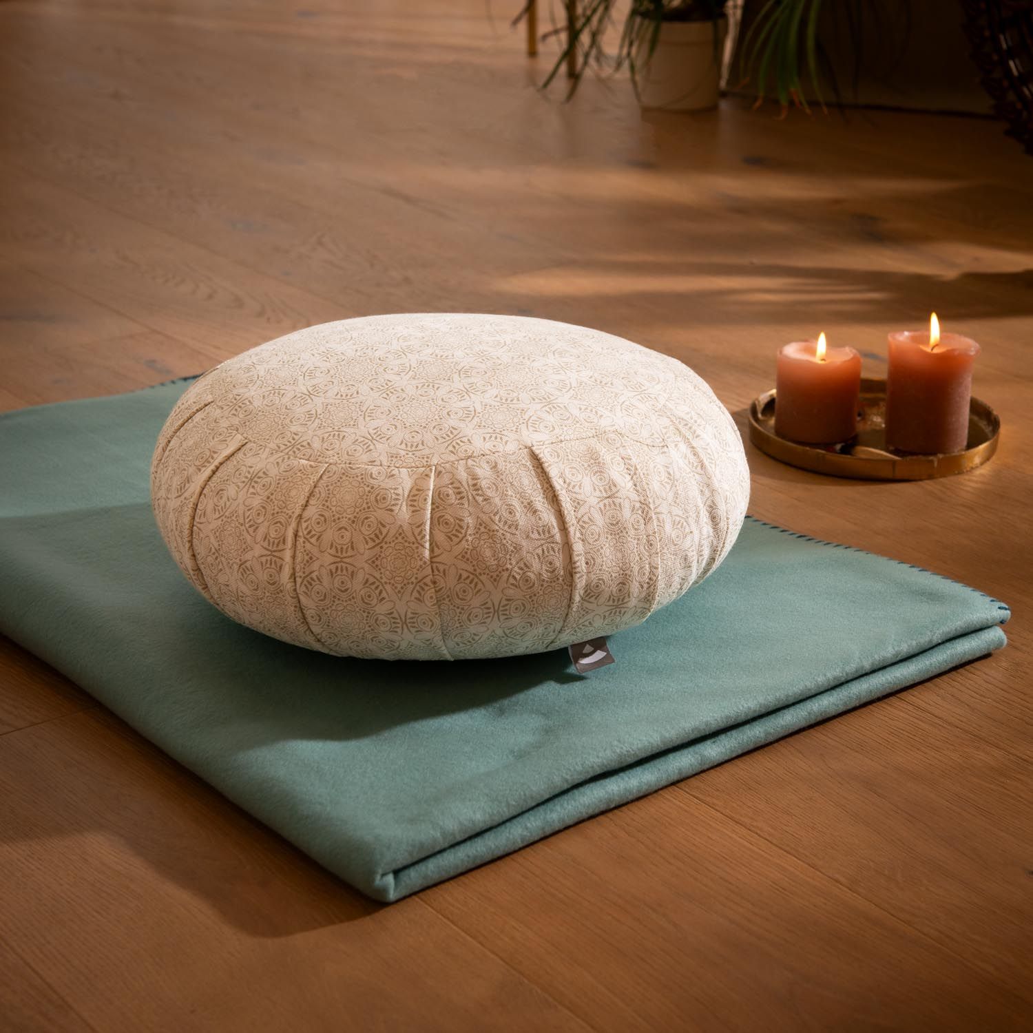Bodhi Zafu Meditationskissen mit Muster auf türkiser Matte, Kerzen im Hintergrund.