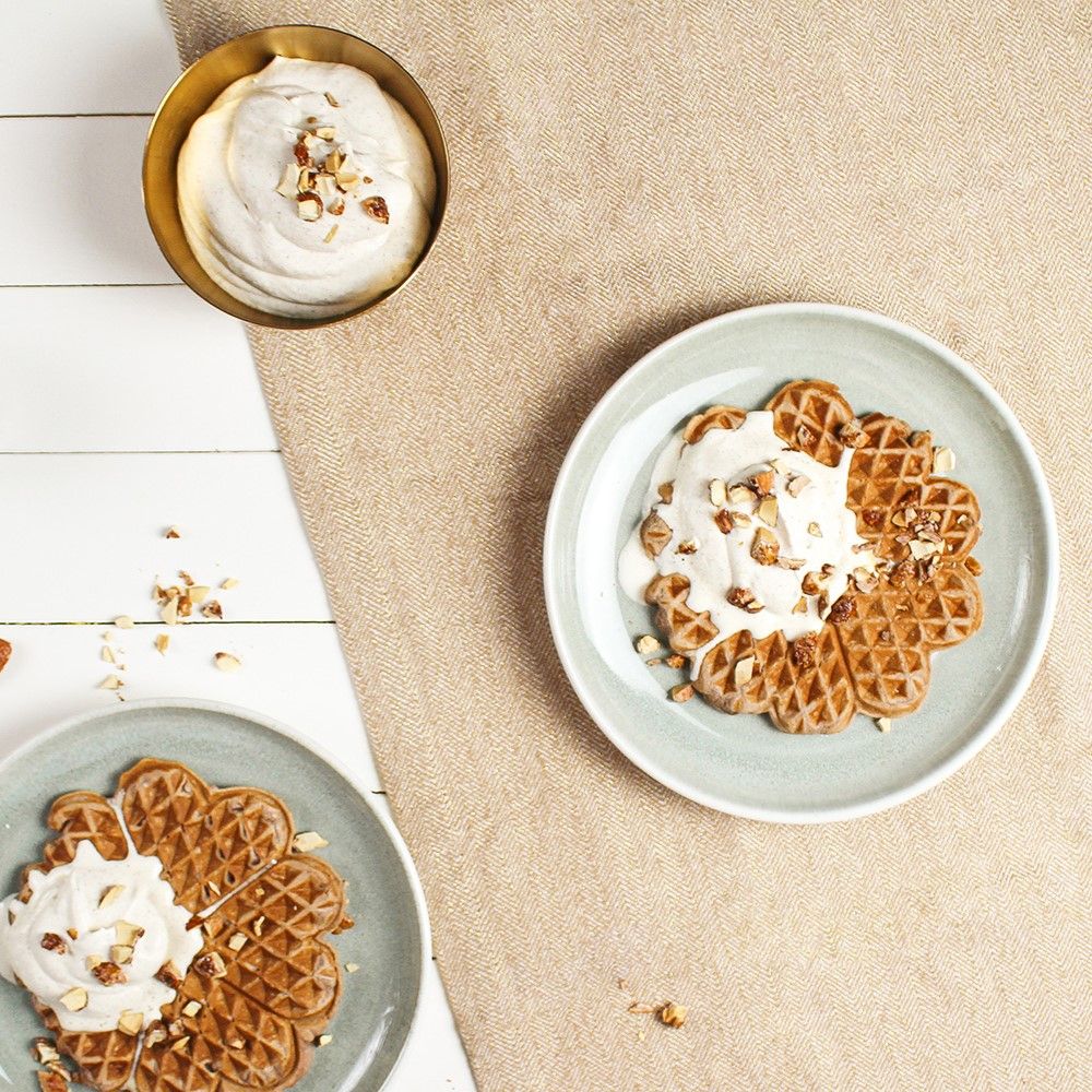 Zwei Teller mit Waffeln und Sahne, Nüssen. Eine Schüssel mit Sahne und Nüssen. Auf hellem Untergrund.