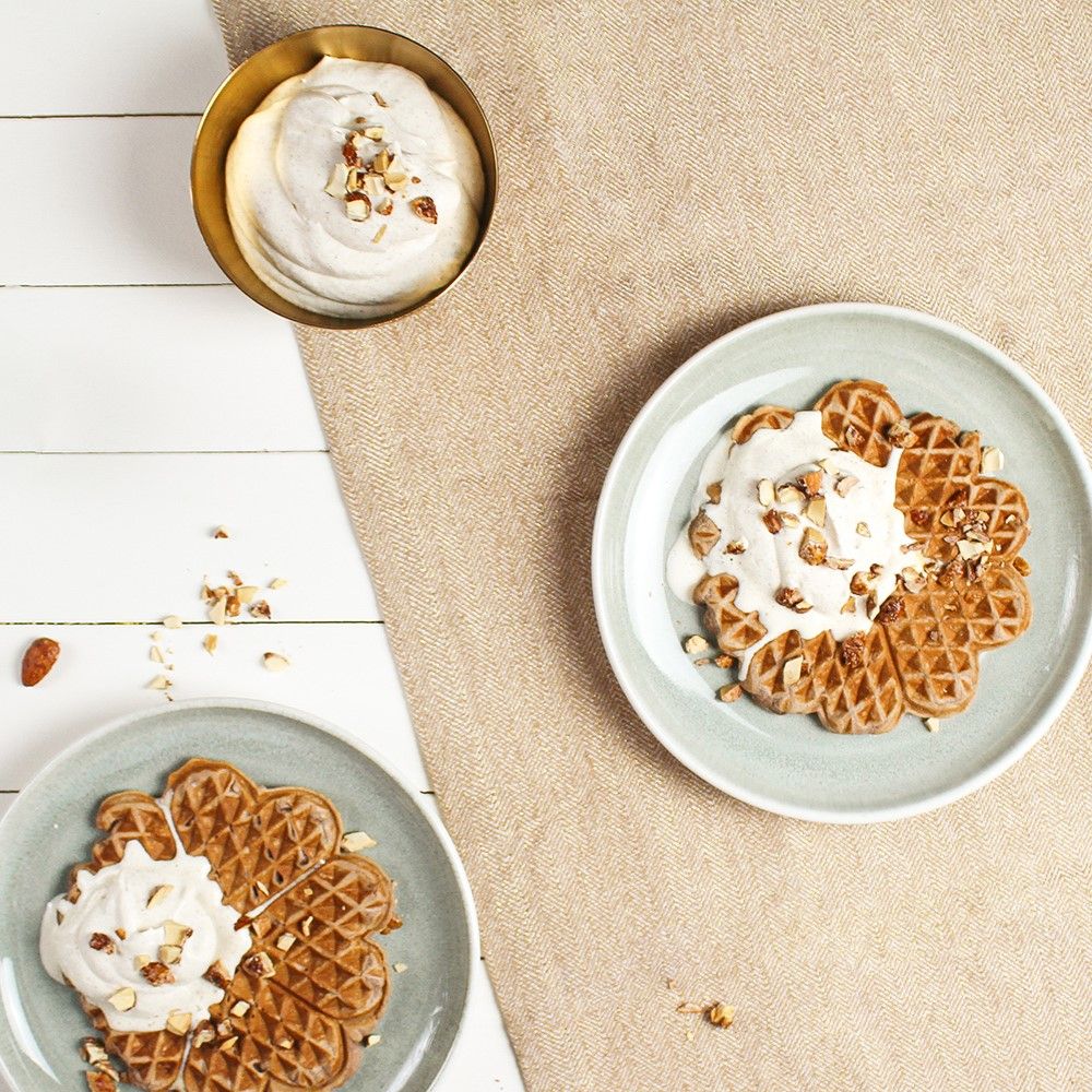 Waffeln mit Creme und Nüssen auf Tellern. Eine Schüssel mit Creme. Auf hellem Holz und Leinen.