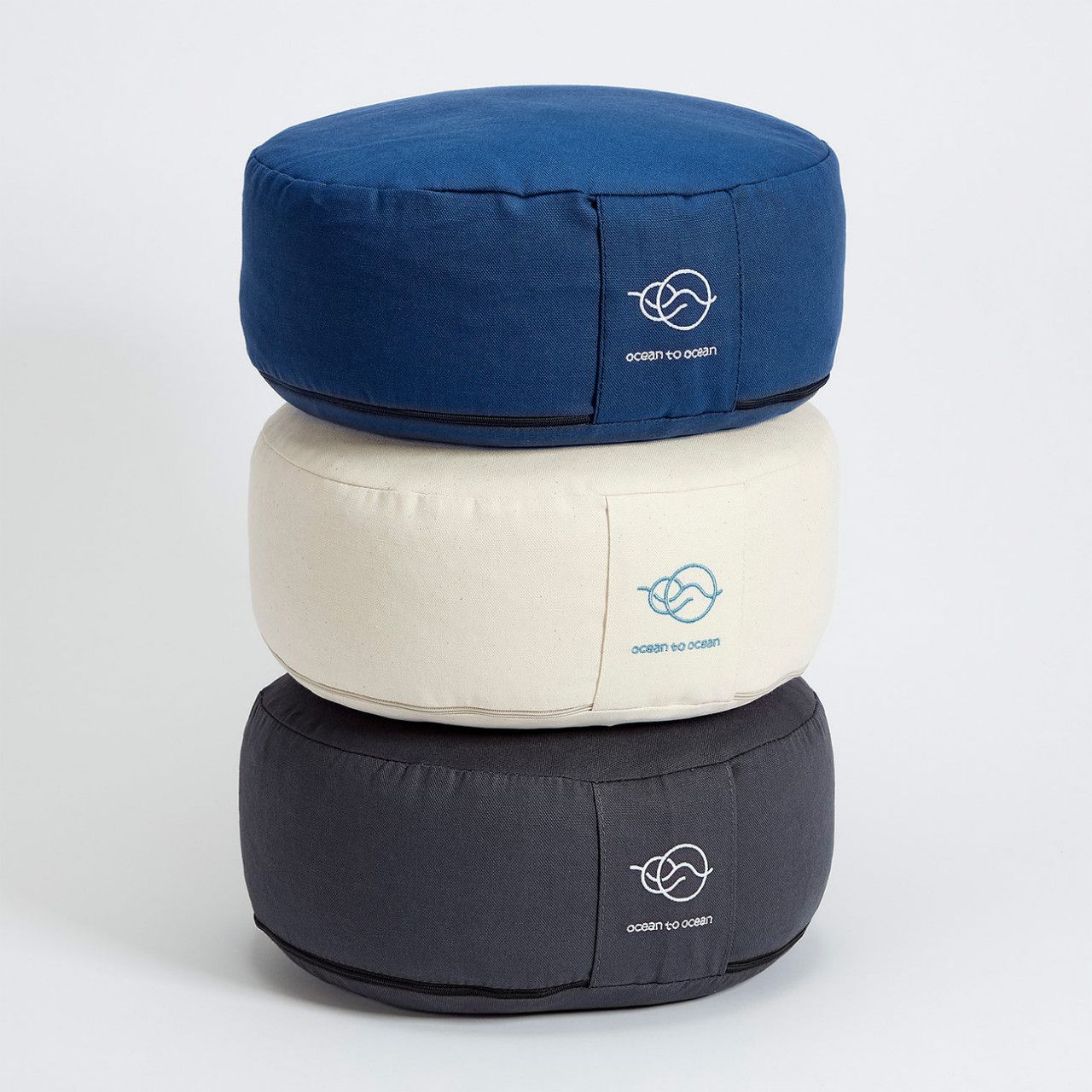 Drei Meditationskissen gestapelt: blau, cremefarben, grau. Mit Logo "ocean to ocean".