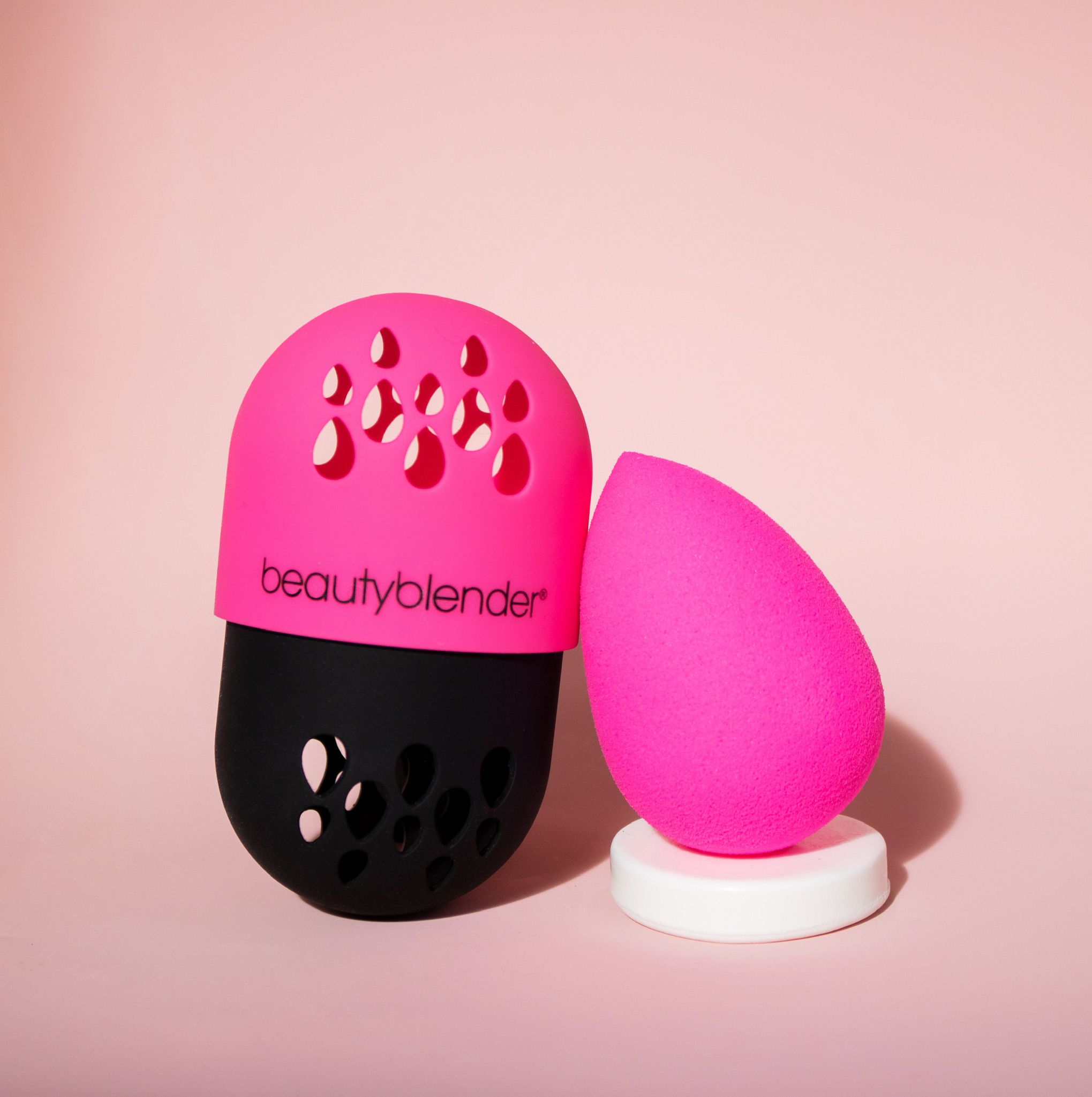 Ein pinkfarbener Beautyblender-Schwamm und ein Halter mit Löchern. Der Halter ist schwarz und pink, mit dem Schriftzug "beautyblender".