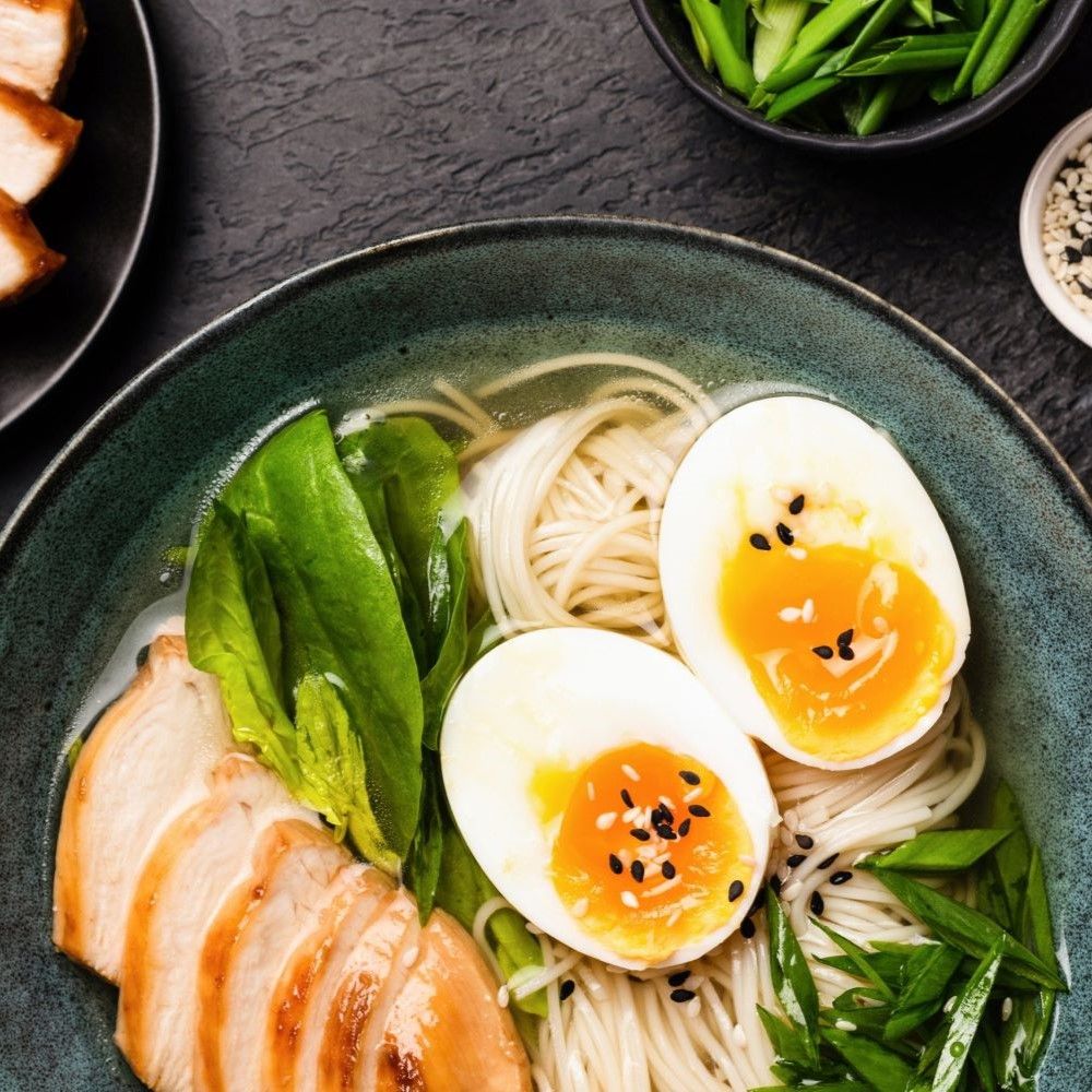 Schüssel mit Ramen-Nudeln, Eiern, Hühnchen und Gemüse. Oben links Hühnchen, rechts Eier, darunter Nudeln.