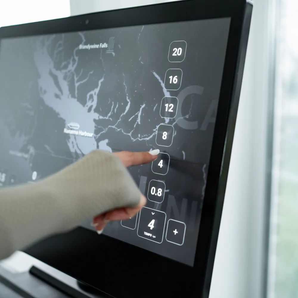 Nahaufnahme des Bildschirms eines Laufbands. Touchscreen mit Zahlen und Karte. Eine Hand berührt den Bildschirm.