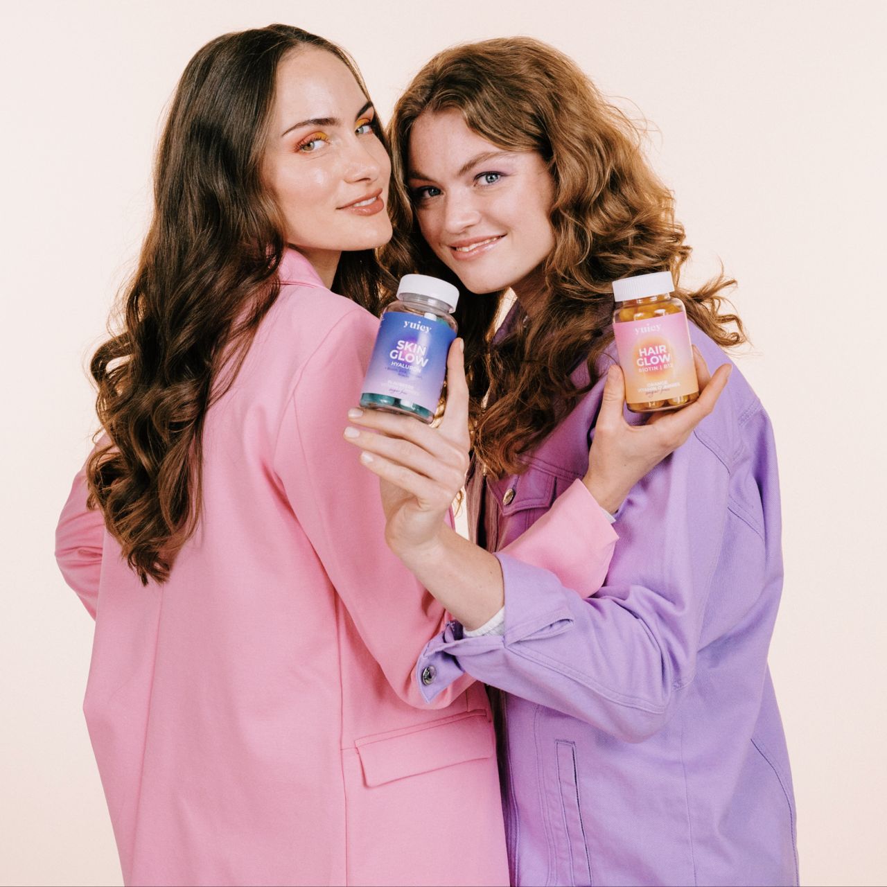 Zwei Frauen halten je eine Flasche yuicy® Vitamin-Gummis. Eine hält Skin Glow, die andere Hair Glow.
