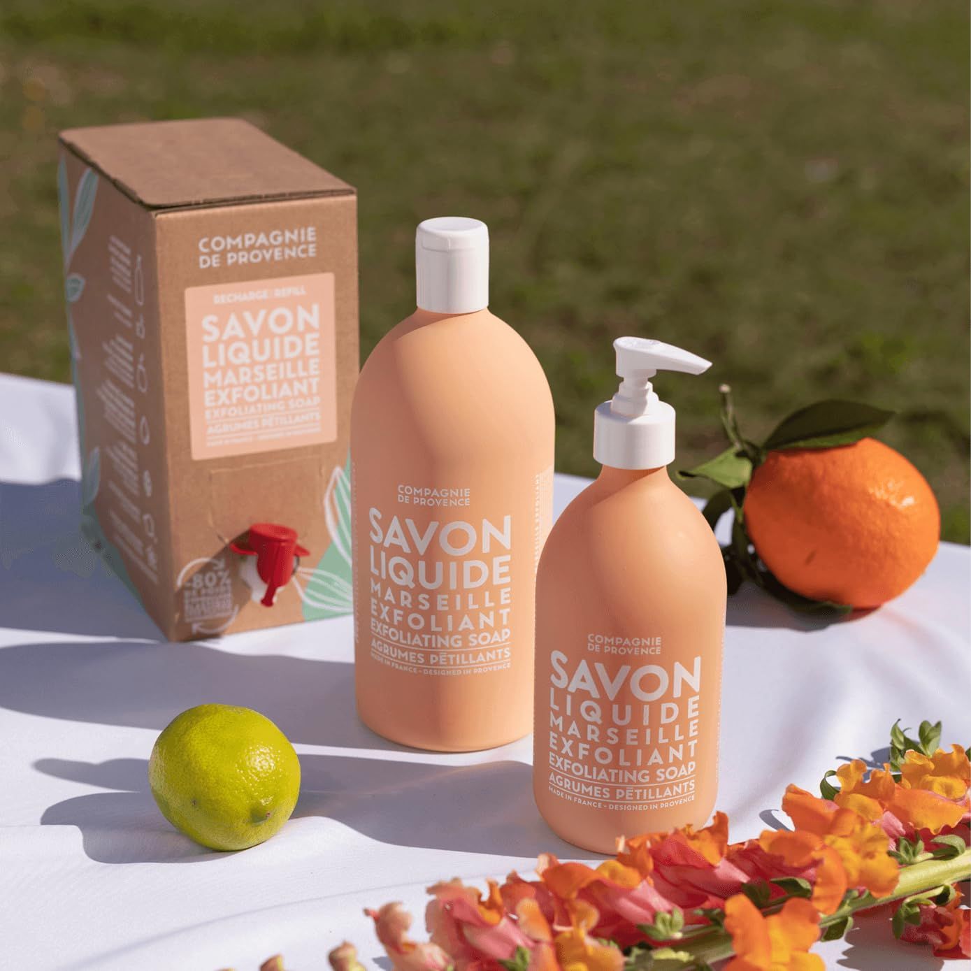 Zwei Flüssigseifenflaschen, eine Schachtel, eine Limette, eine Orange und Blumen.