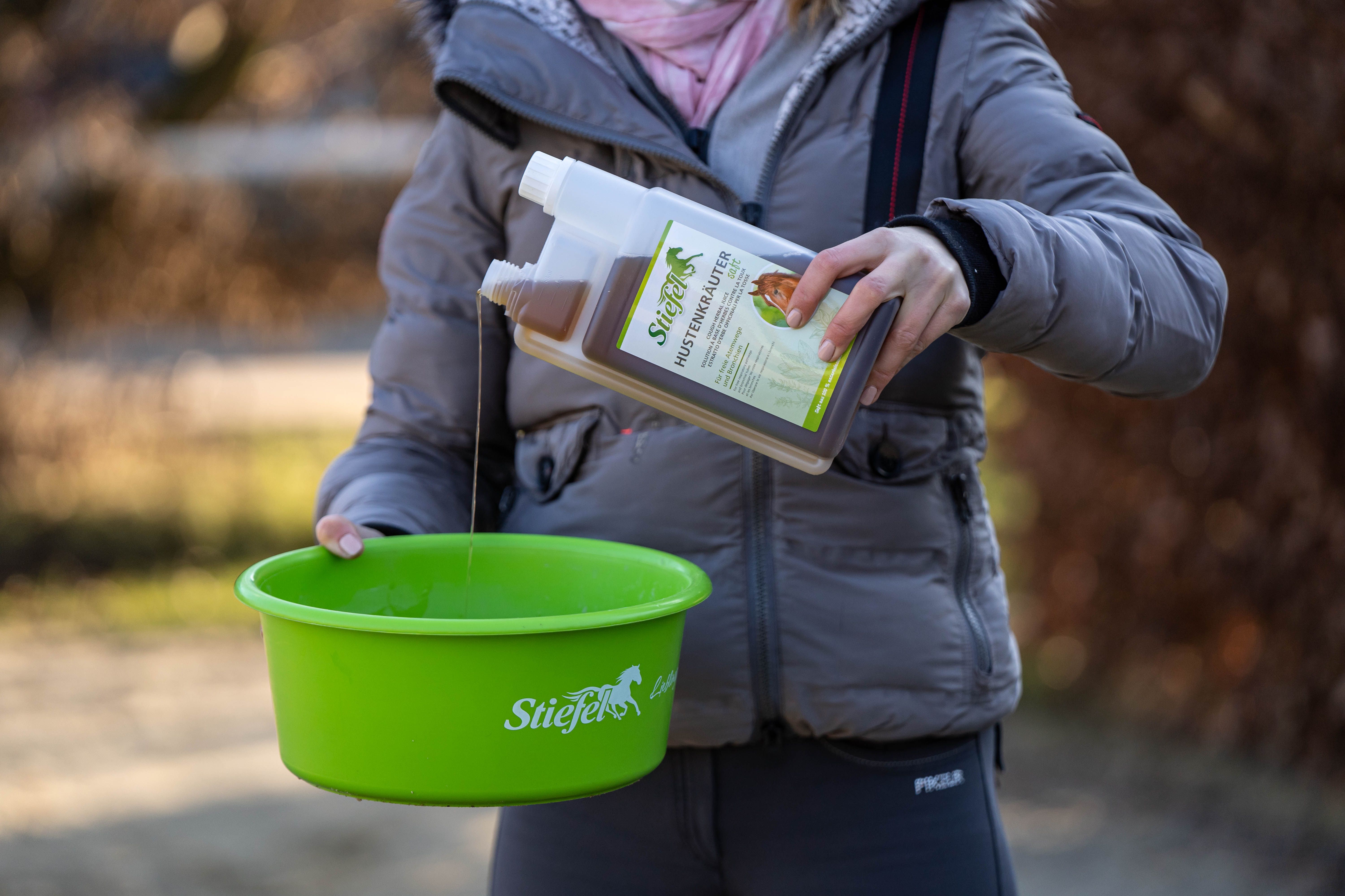 Person gießt braune Flüssigkeit aus einer Flasche in eine grüne Schüssel. Auf der Flasche steht der Produktname. Die Schüssel hat einen grünen Rand.