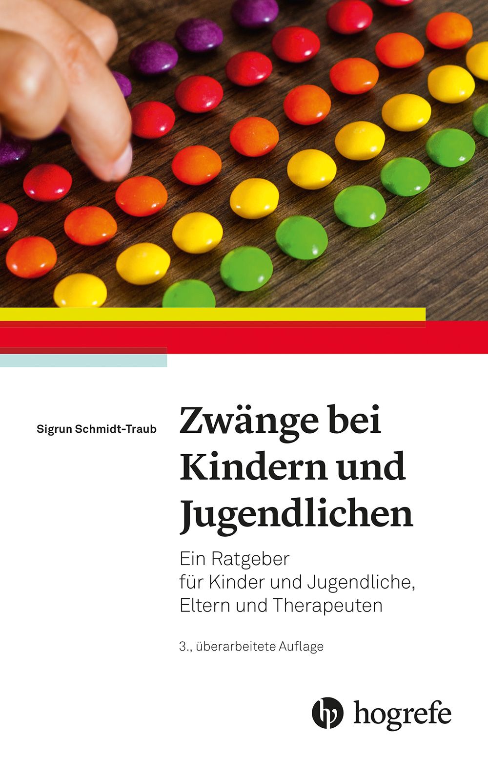 Buchcover: "Zwänge bei Kindern und Jugendlichen". Titel, Autor, Verlag Hogrefe. Bunte, runde Objekte auf Holzgrund.
