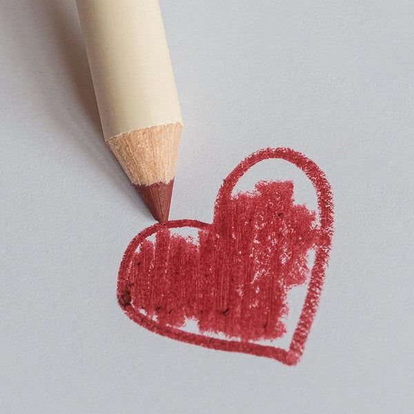 Roter Lippenstiftstift zeichnet ein Herz auf weißem Papier.