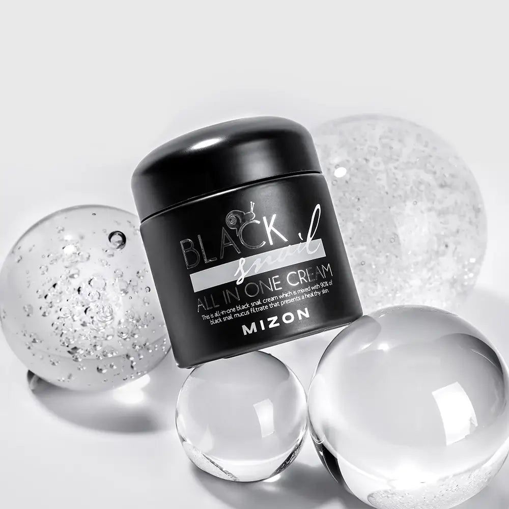 Schwarzer Tiegel mit schwarzem Deckel. Aufschrift: BLACK snail ALL IN ONE CREAM. Umgeben von transparenten Kugeln.