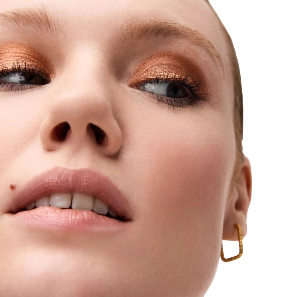 Nahaufnahme eines Gesichts mit goldfarbenem Lidschatten. Hautton hell, Augenbrauen und Lippen natürlich.