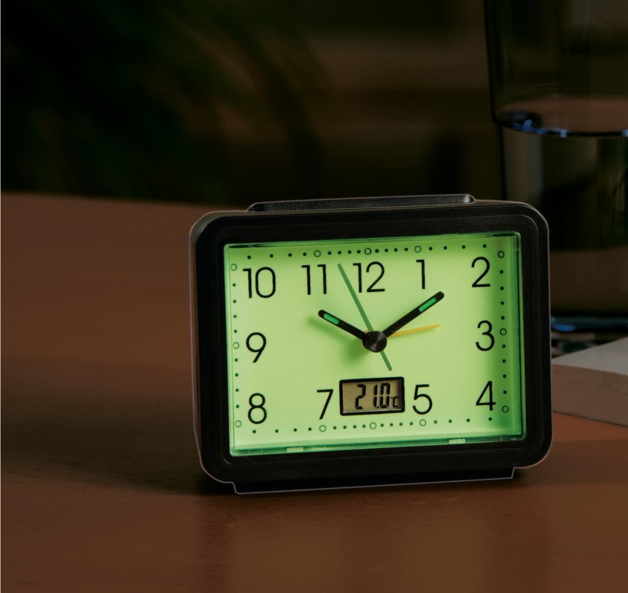 Rechteckiger Wecker mit schwarzem Rahmen, grün leuchtendem Zifferblatt. Schwarze Zeiger, digitale Anzeige. Ziffern von 1 bis 12.