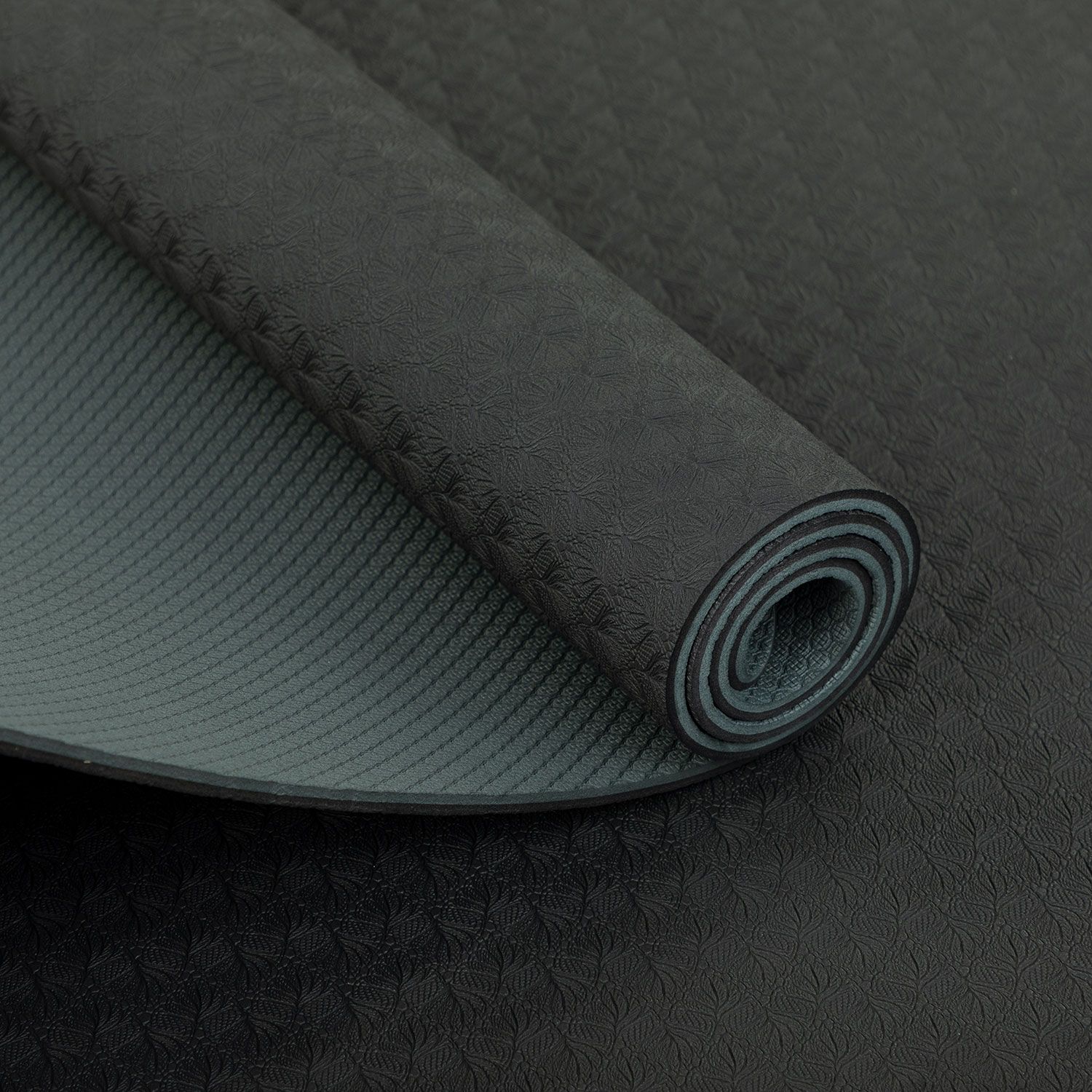 Nahaufnahme einer gerollten Yogamatte. Anthrazitfarbene Oberseite mit Muster, graue Unterseite.