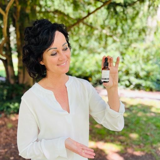 Frau hält Produktflasche. Flasche mit Text: CERTIFIED ORGANIC ILLUMINATING SERUM. Frau lächelt.