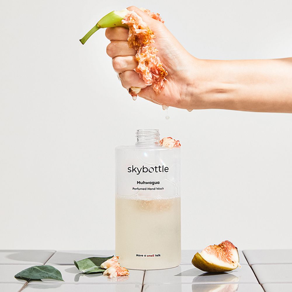 Flasche mit Seife, Feigen und Hand. Aufschrift: skybottle, Muhwagua, Perfumed Hand Wash. Grauer Hintergrund.