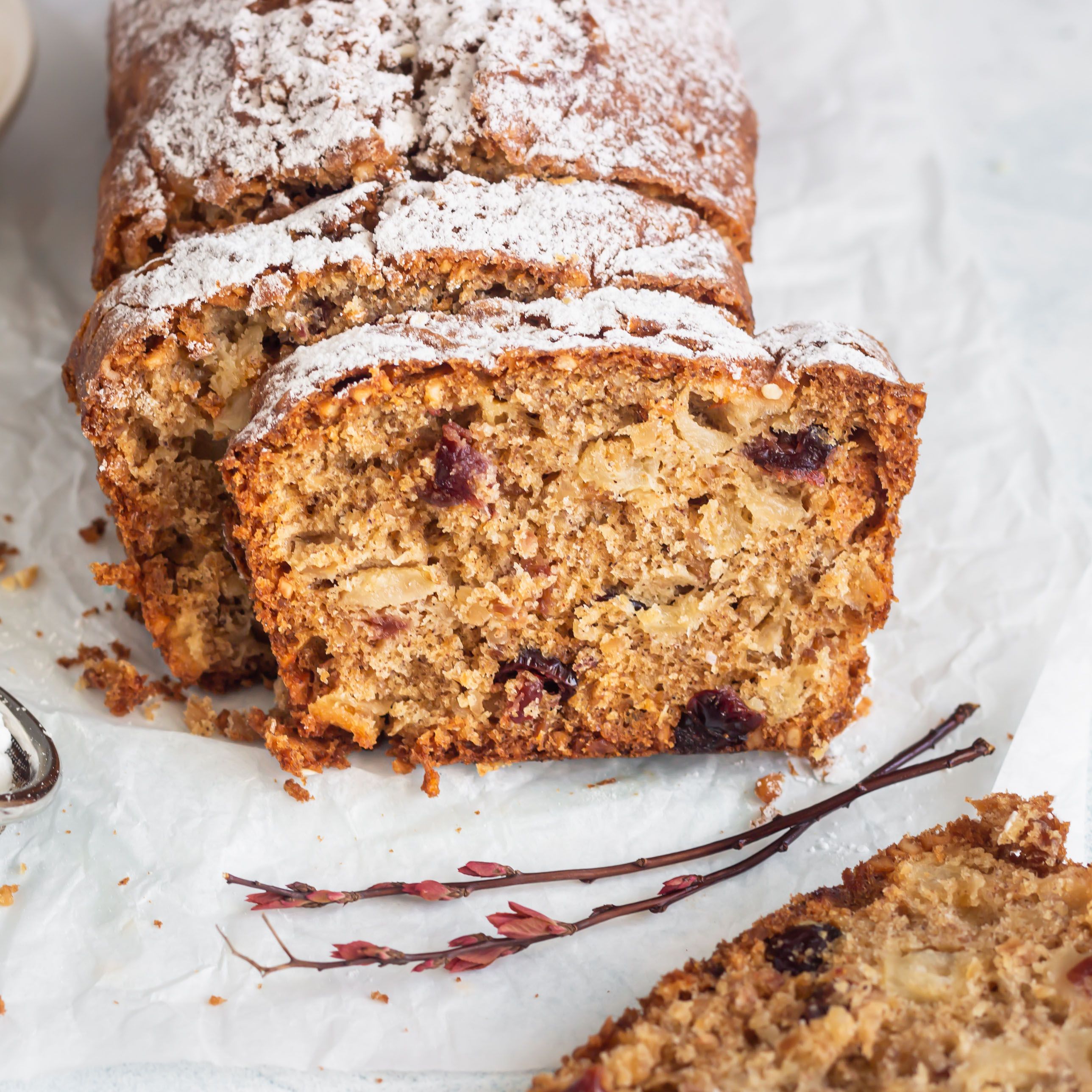 Geschnittenes Brot mit Äpfeln und Cranberries. Mit Puderzucker bestäubt. Auf weißem Papier. Dekoriert mit Zweigen.