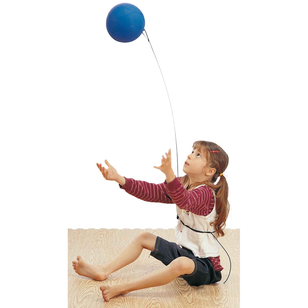 Kind sitzt und greift nach blauem Ball. Ball an Schnur. Kind trägt Oberteil.