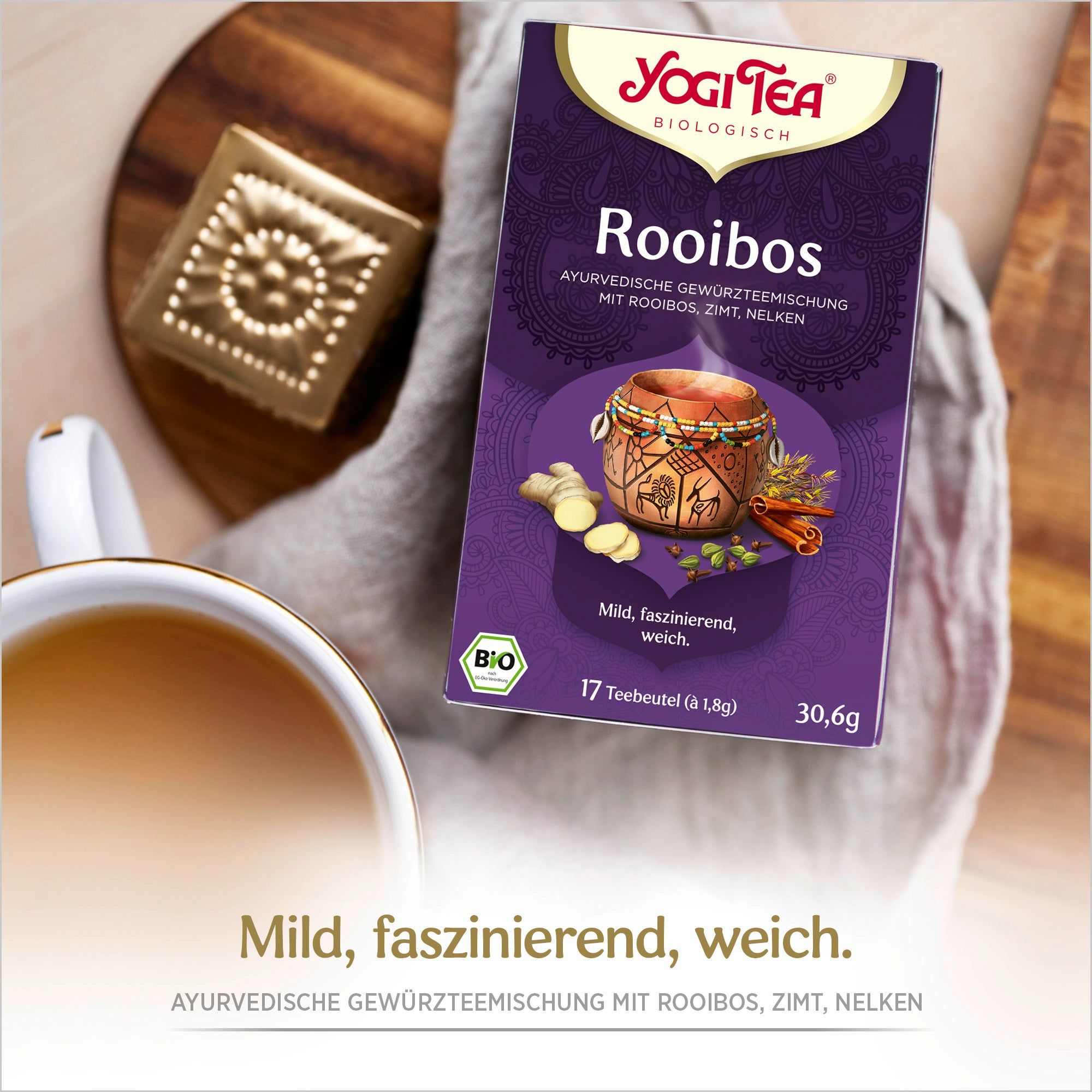 Yogi Tea Rooibos Packung auf Holzbrett. Logo, Produktname und Zutaten. Bio-Siegel. Tasse Tee daneben.