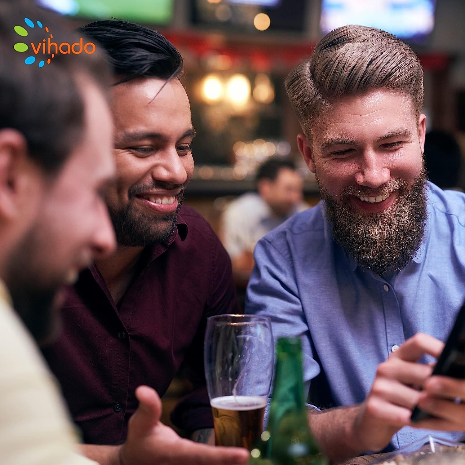 Drei Männer sitzen an einem Tisch und schauen auf ein Smartphone. Im Hintergrund eine Bar.
