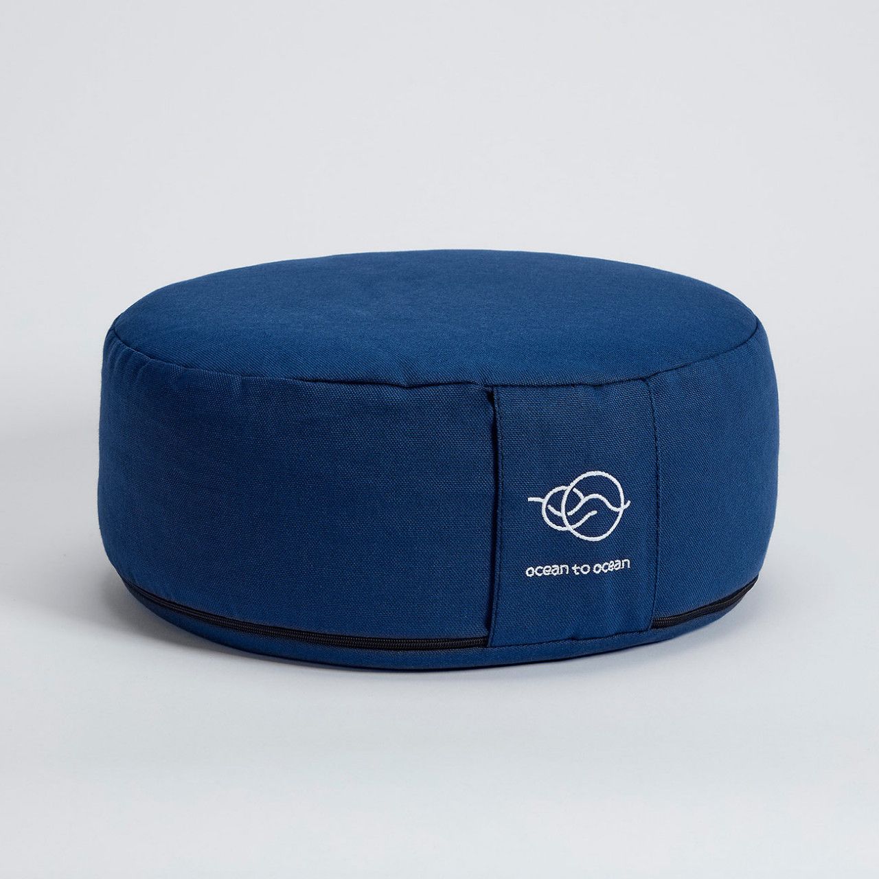 Blaues, rundes Meditationskissen mit weißem Logo und Schriftzug "ocean to ocean". Schwarzer Reißverschluss.