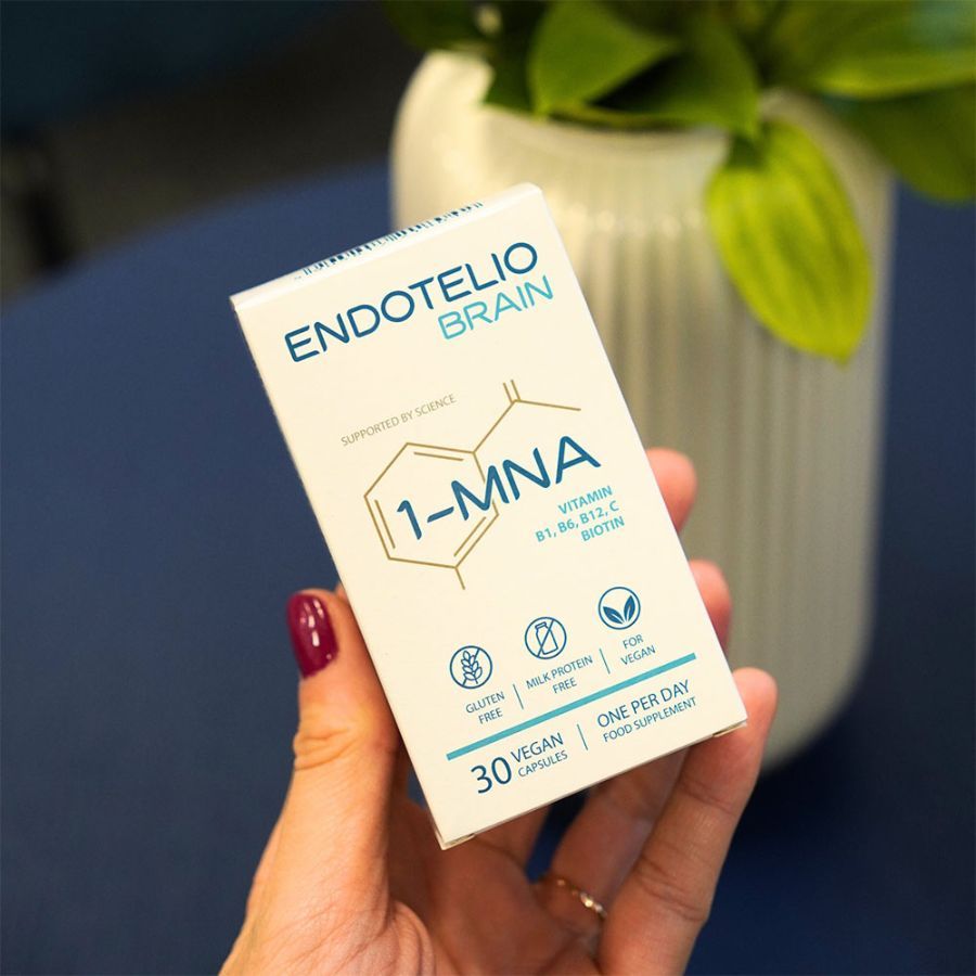 Hand hält eine Produktverpackung. Aufschrift: ENDOTELIO BRAIN, 1-MNA, 30 vegane Kapseln. Glutenfrei, milchproteinfrei, vegan.