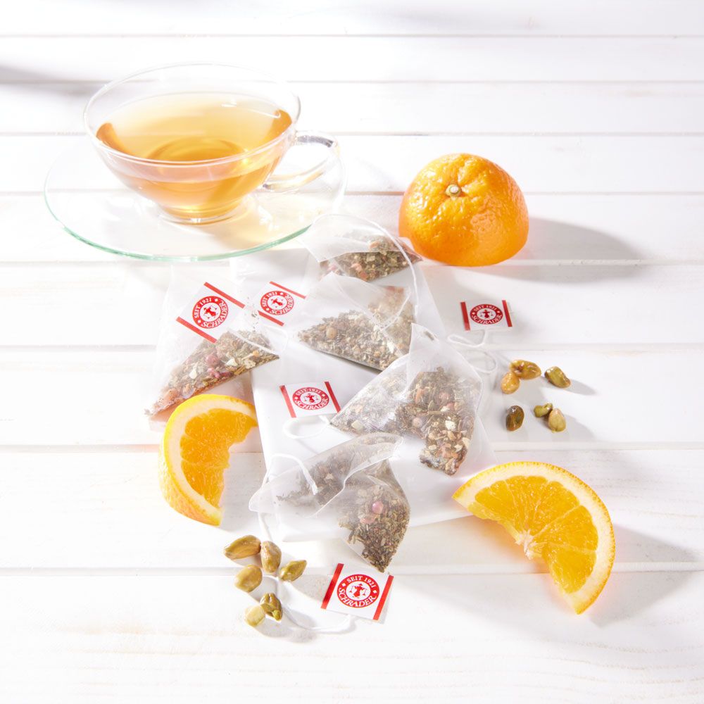 Teebeutel mit Kräutern, Orangenstücke, Pistazien und eine Tasse Tee. Auf weißem Holzgrund.