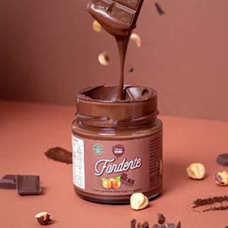 Vasetto di crema al cioccolato "Fondente". Nocciole e pezzi di cioccolato intorno al vasetto. Cioccolato che cola.