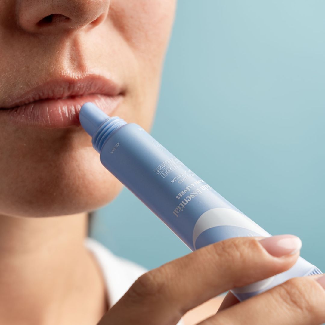 Person trägt hellblaue Tubenlippenpflege auf. Nahaufnahme der Lippen. Produktname und Schriftzug sichtbar.