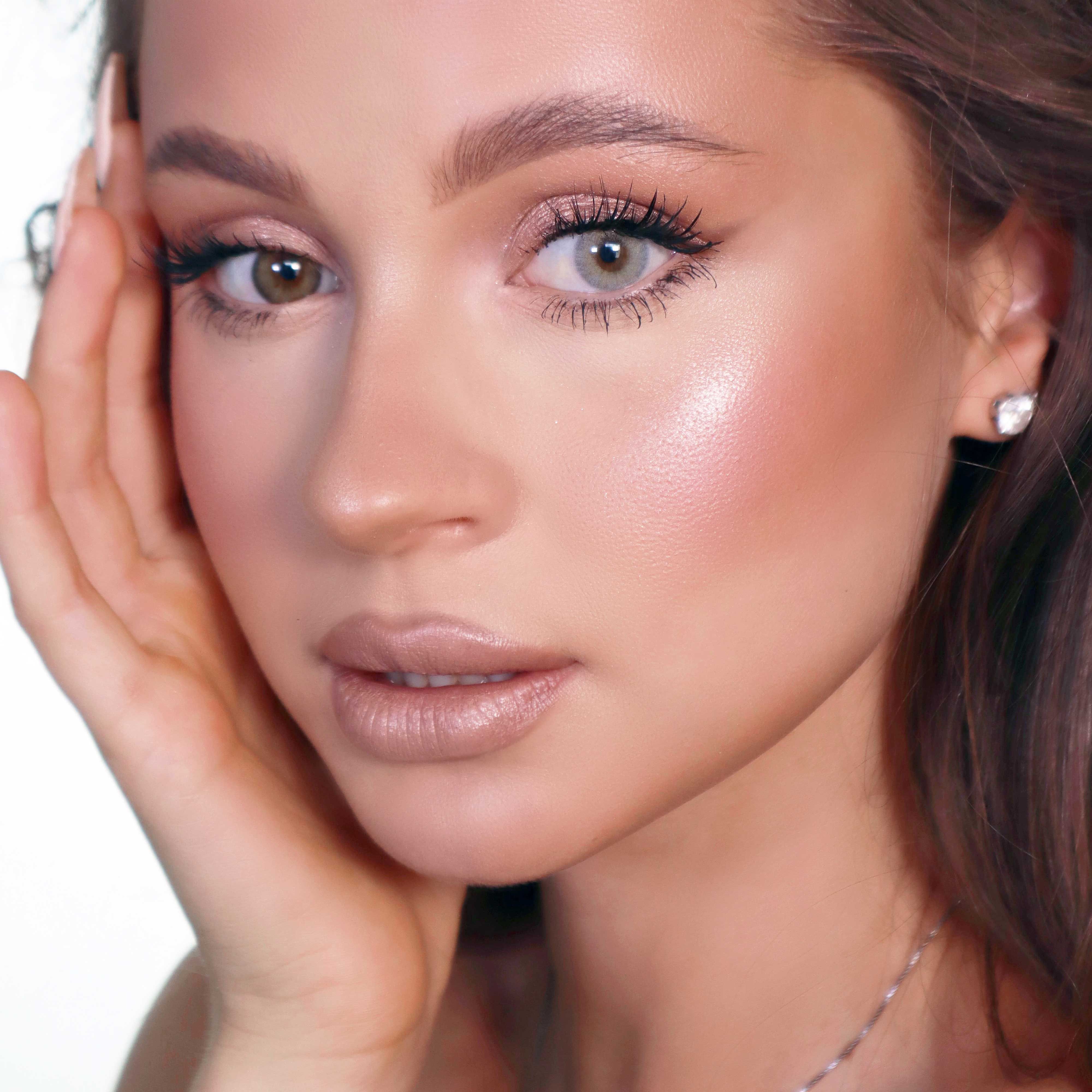 Porträt einer Frau mit grauer Kontaktlinse im rechten Auge. Sie berührt ihr Gesicht mit der Hand.