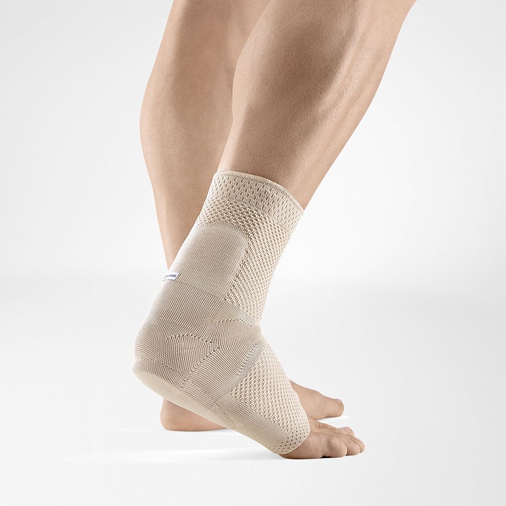 Beige Knöchelbandage am Fuß. Gestricktes Material, gepolsterte Bereiche. Angedeuteter Markenname.