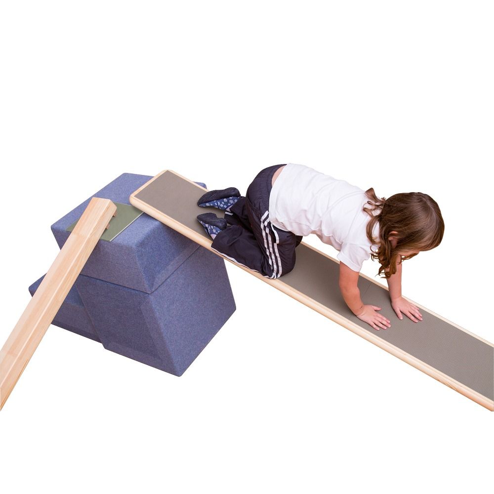 Kind klettert auf einer schrägen Rampe. Die Rampe ist mit Holz umrandet und liegt auf blauen Schaumstoffblöcken. Ein weiteres Holzteil liegt daneben.