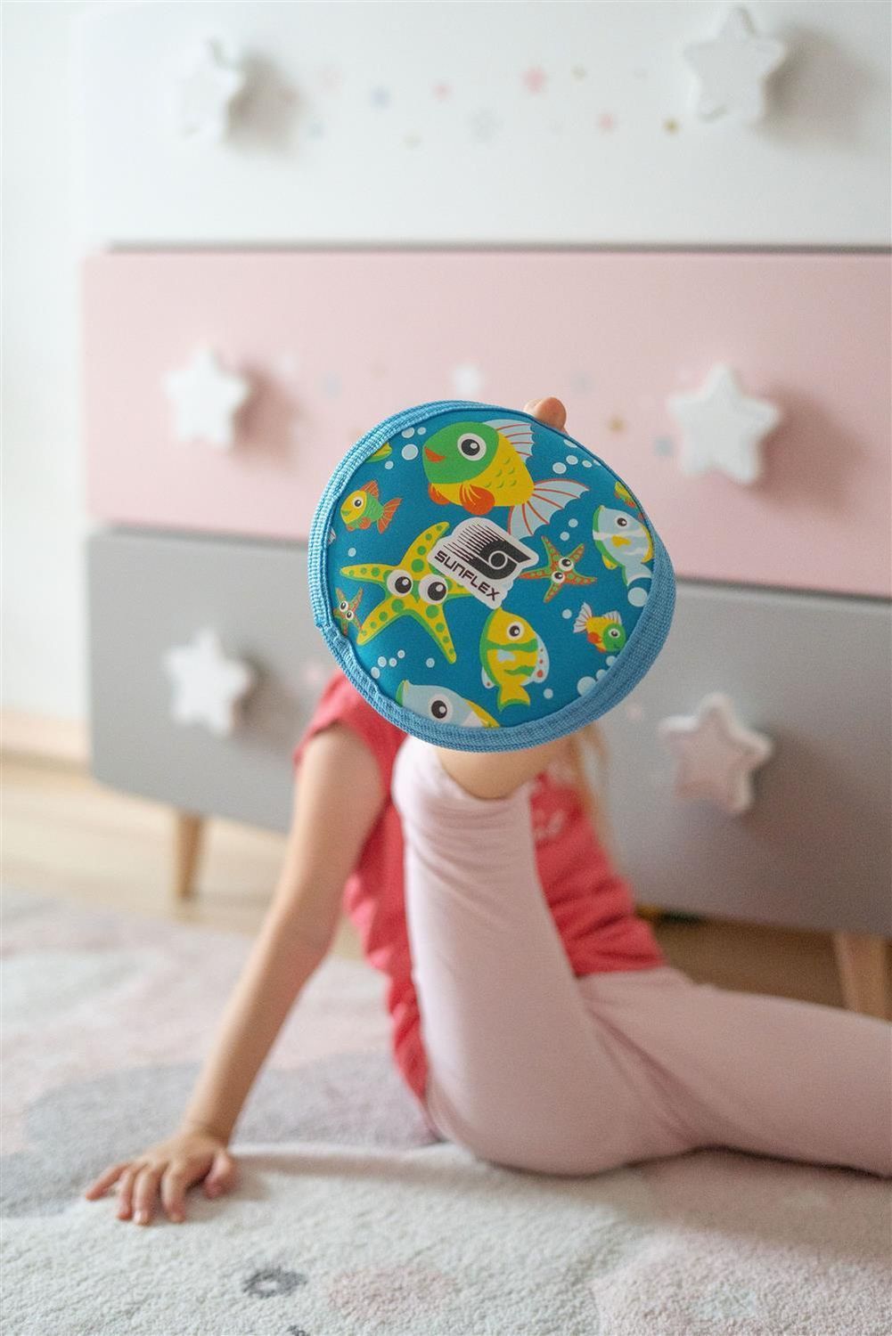 Kind hält Sunflex Uranus Youngster Seaworld. Blau mit Fisch- und Seestern-Motiven. Kind sitzt auf dem Boden.