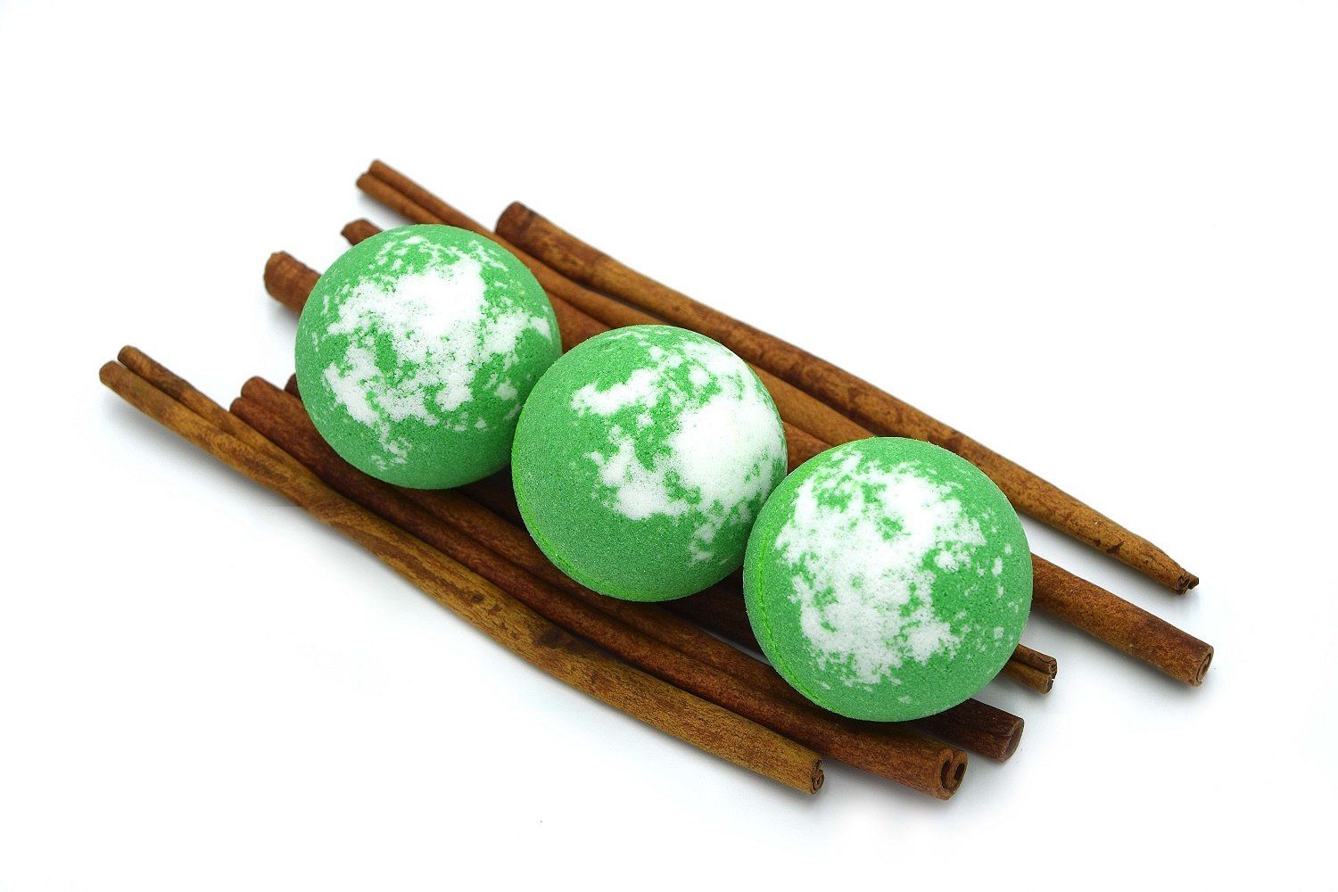 Drei grüne, runde Badebomben mit weißen Flecken, auf Zimtstangen platziert. Auf weißem Hintergrund.