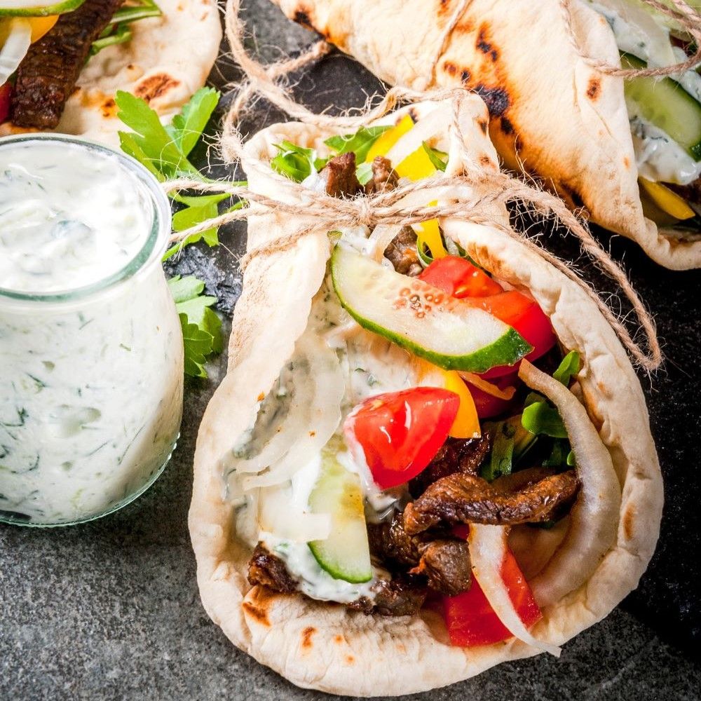 Fladenbrot gefüllt mit Gemüse und Fleisch. Daneben ein Glas mit Sauce.