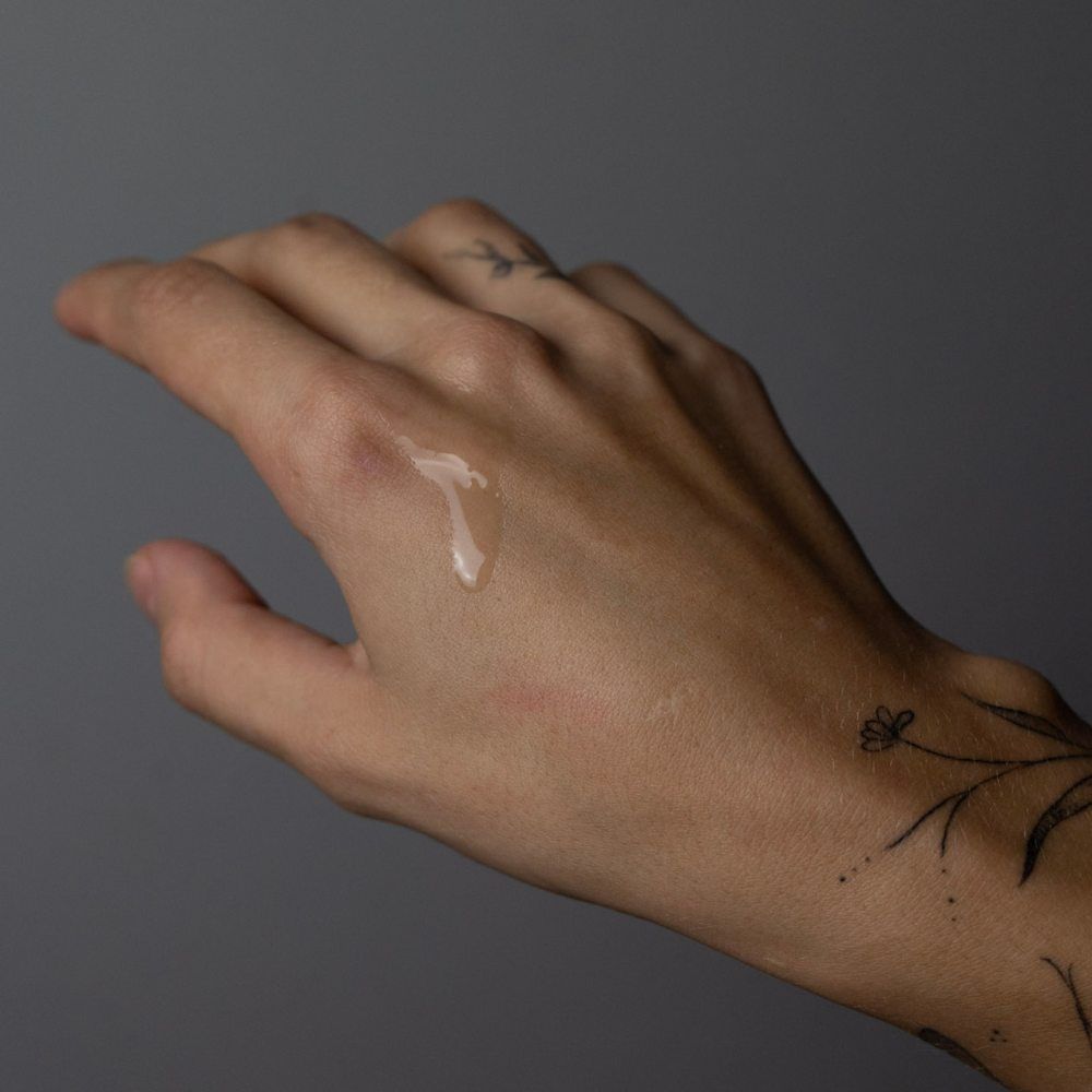 Hand mit Öl. Klare Flüssigkeit auf der Haut. Hintergrund grau.