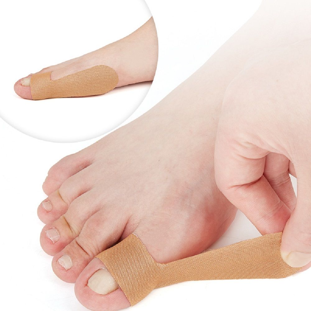 Person bringt ein beiges Daumenstützband an einem Zeh an. Band um den Zeh gewickelt. Nahaufnahme des Fußes.