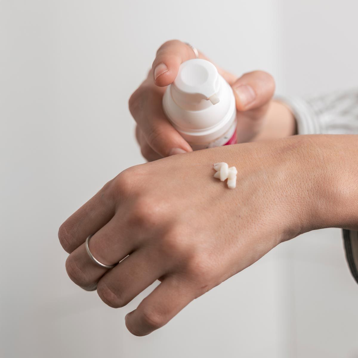 Person hält eine weiße Pumpflasche und gibt Lotion auf die Hand. Creme-Tropfen auf der Haut sichtbar.
