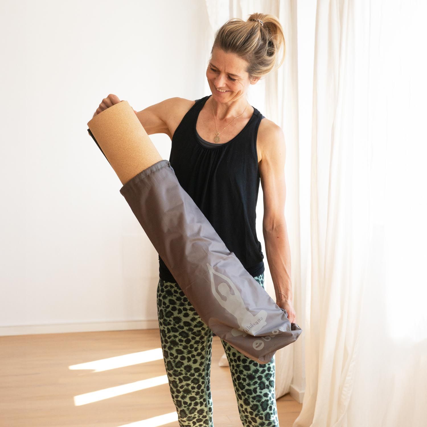 Frau hält eine graue Yogamattentasche. Sie öffnet die Tasche, um eine Yogamatte zu entnehmen.