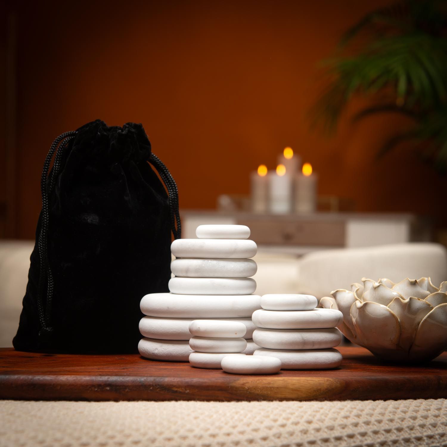 Weiße, ovale Steine und eine schwarze Tasche auf einem Tisch. Kerzen im Hintergrund.