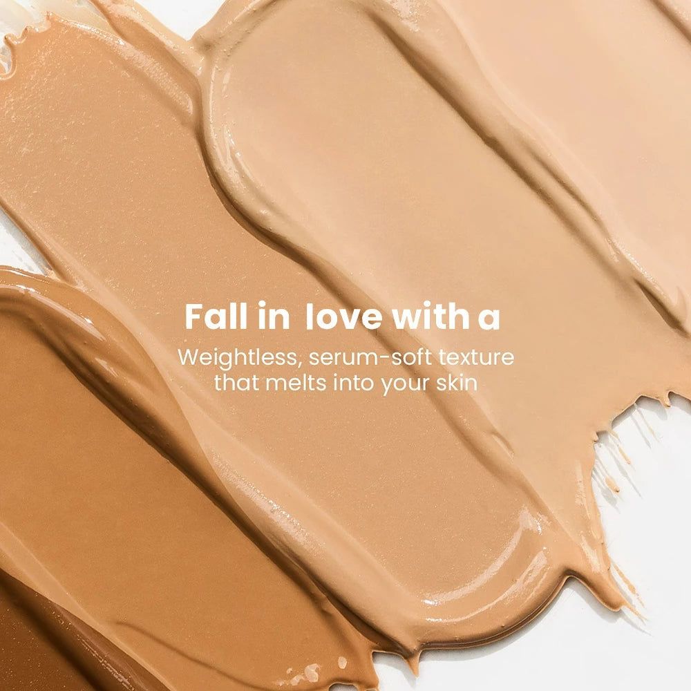 Mehrere Swatches von flüssiger Foundation in verschiedenen Hauttönen, die auf einer weißen Oberfläche verteilt sind.