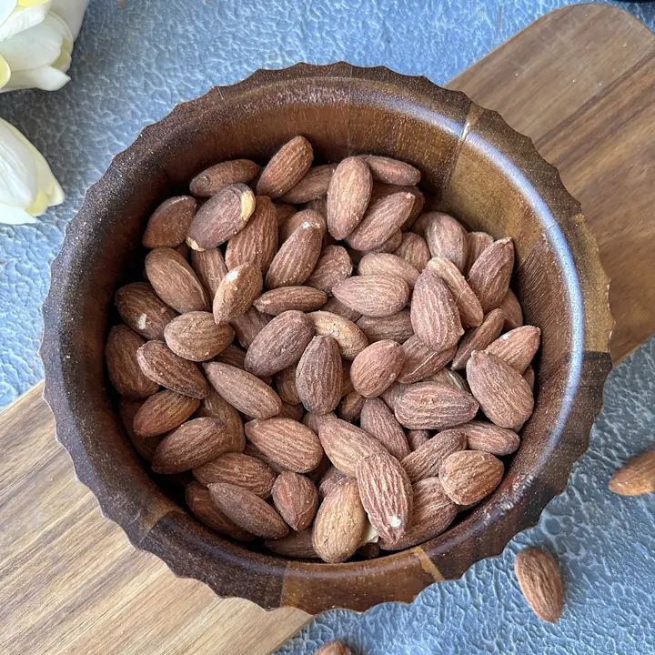 Mandeln in einer Holzschale. Die Schale steht auf einem Holzbrett. Nahaufnahme von oben.