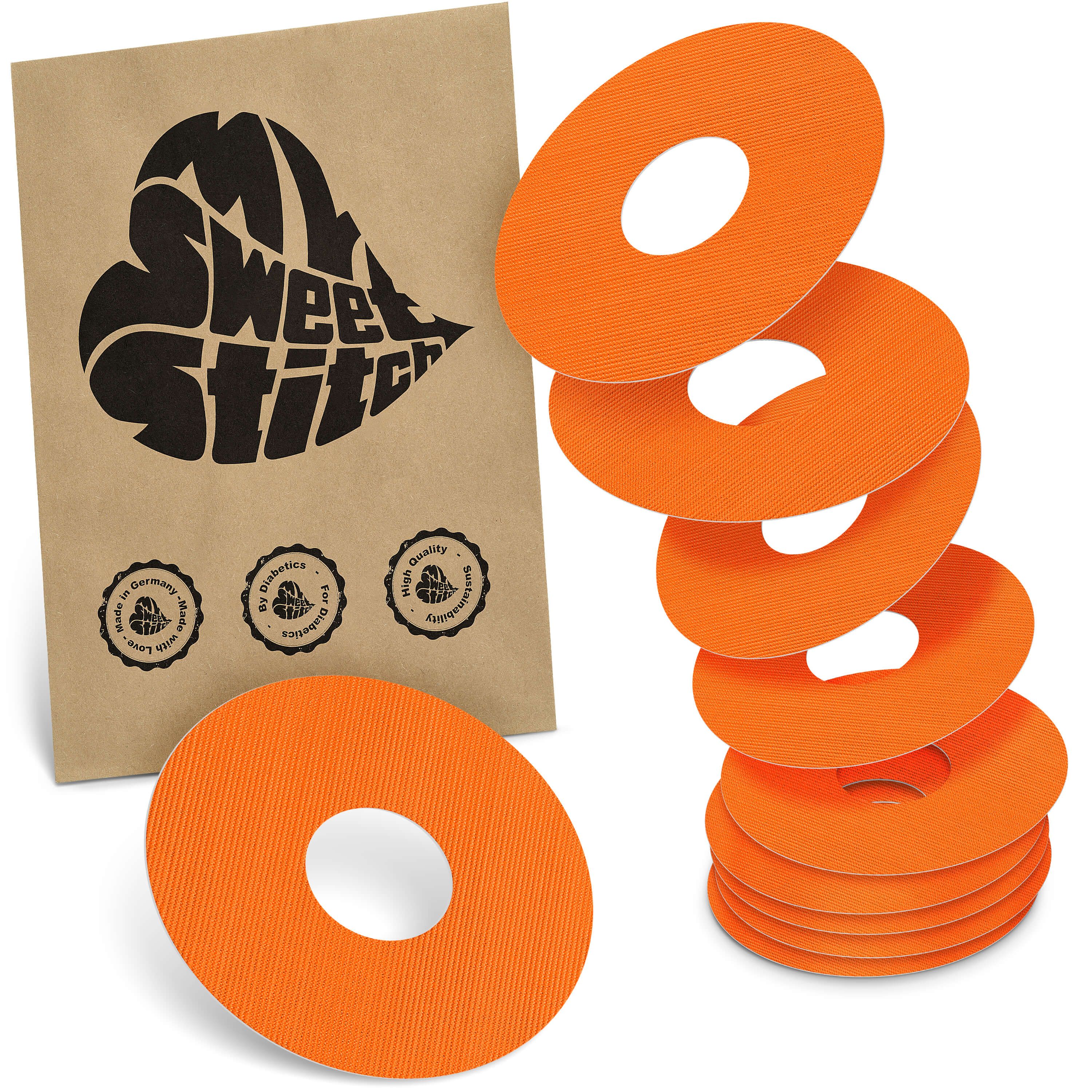 Orange Ringpflaster mit zentralem Loch, gestapelt und einzeln. Braune Verpackung mit Logo.