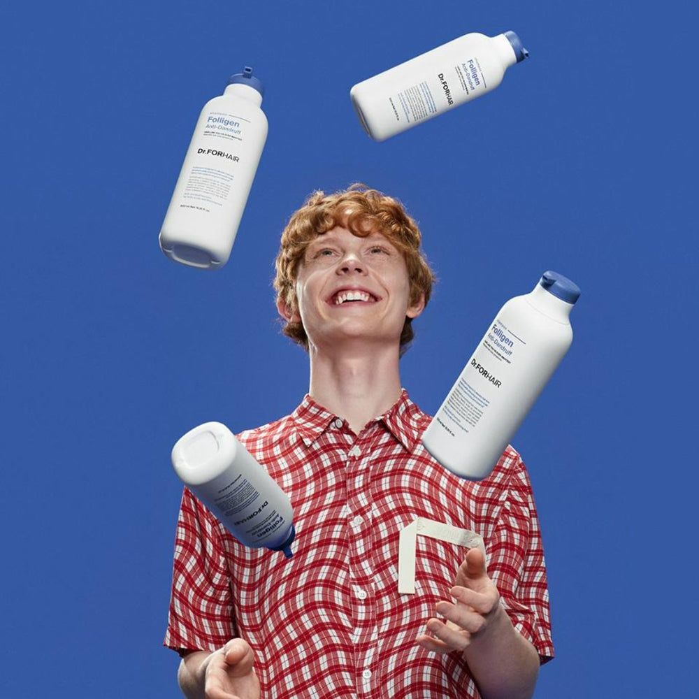 Ein Mann jongliert mit vier Flaschen Dr. FORHAIR Folligen Anti-Schuppen-Shampoo vor einem blauen Hintergrund.
