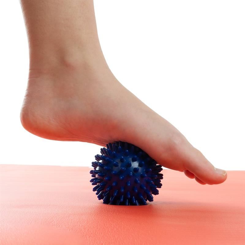 Fuß auf einem blauen Massageball mit Noppen. Der Fuß steht auf einer roten Matte.
